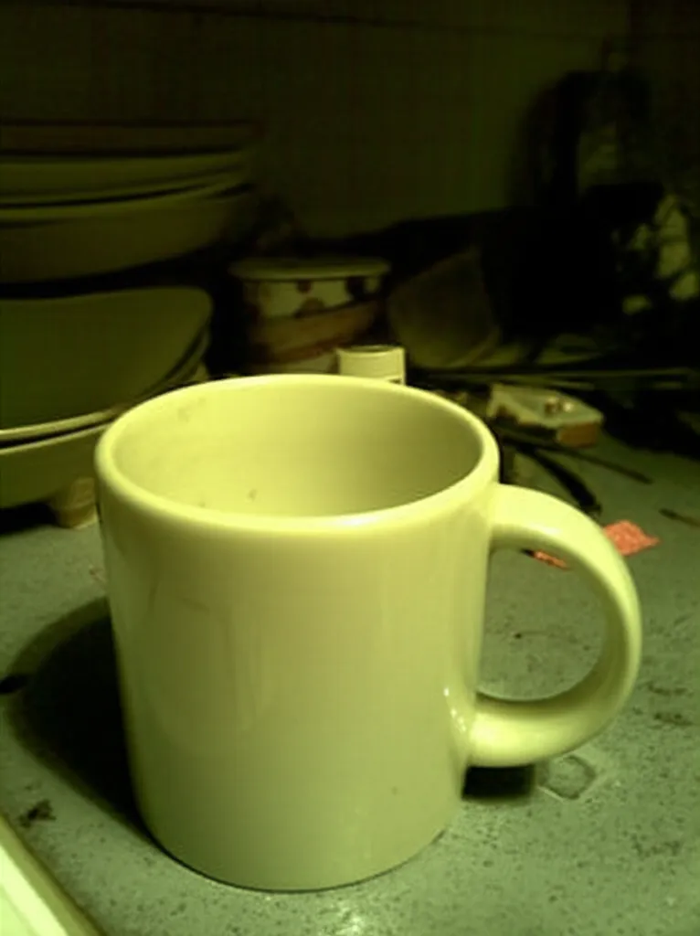 Poorly lit product photo of a ceramic mug with cluttered background and harsh shadows