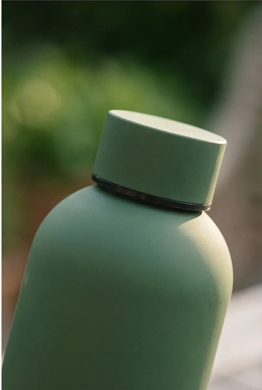 AI lifestyle photo: water bottle beside laptop with plants in background